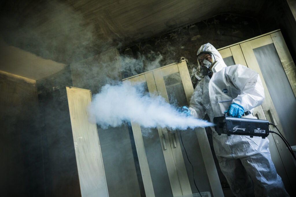 A technician using a fog machine during a smoke odour removal service in a domestic property.