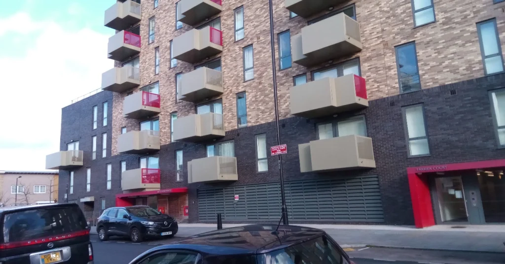 The outside of a block of new London flats with balconies and cars parked on the street.