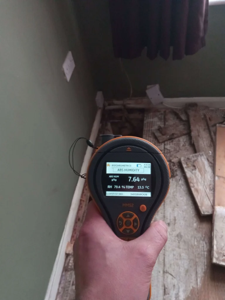 A technicians hand holding a damp meter, measuring the moisture levels of a floor void in a domestic property.