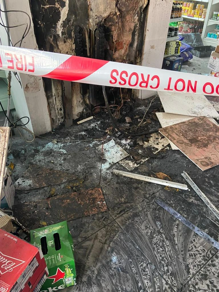 Soot and fire damaged retail unit with red and white tape blocking the entrance.