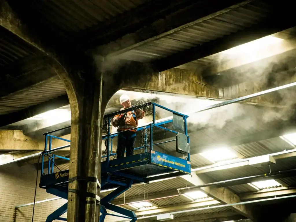 Technician on top of a scissor lift using a pressure washer to clean the ceiling of a commercial building.