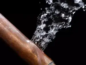 A burst copper pipe with water spraying out of it.