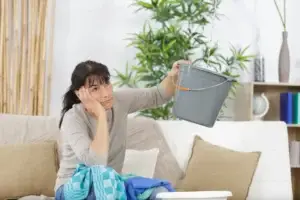 Female holding bucket to catch water from ceiling